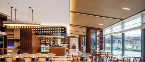 A spacious hotel lobby with a bar area, seating arrangements, and large windows providing a view.
