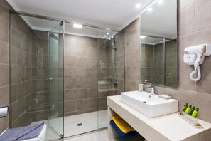 Un baño moderno con cabina de ducha de vidrio, un lavabo blanco y un secador de pelo montado en la pared.