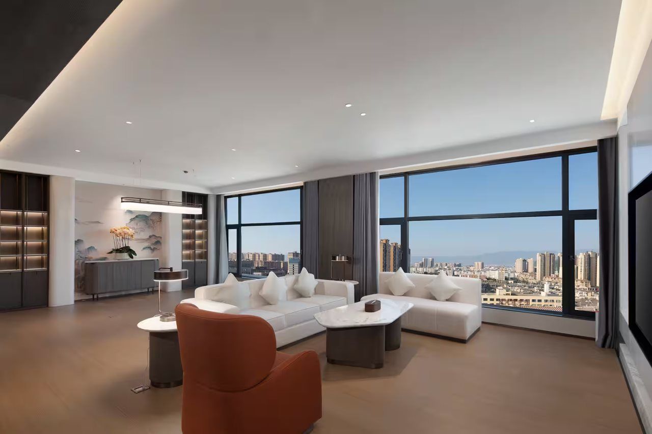 A modern living room with a sofa, coffee table, and a view of a cityscape through large windows.