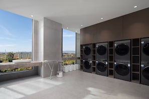 A modern laundry room with multiple washing machines, a drying rack, and a view of the cityscape. - Wyndham Qujing Luliang (Qujing)