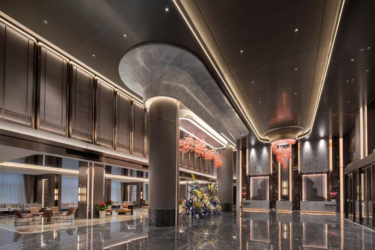 A spacious lobby with a high ceiling, polished marble floors, and modern lighting fixtures.