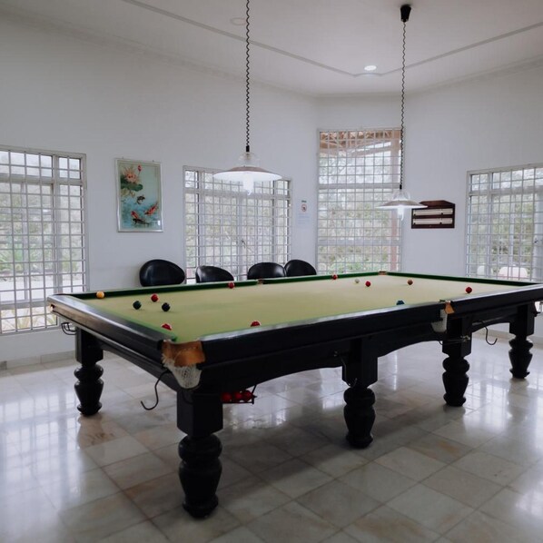 A pool table with a green felt surface, surrounded by black legs, in a room with white walls and large windows.
