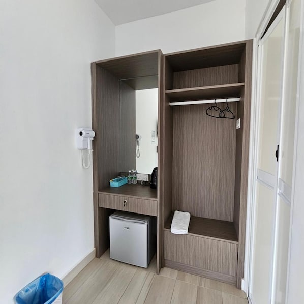 A compact room with a built-in wardrobe, a small fridge, a mirror, and a towel rack.