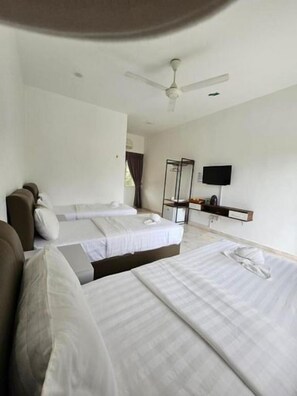 A hotel room with two beds, a sofa, a flat-screen TV, and a ceiling fan.