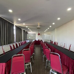 A conference room with a long table, red chairs, a whiteboard, and a projector screen.