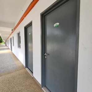 A row of dark-colored doors with a green sticker on one, a covered walkway, and a gravel path.