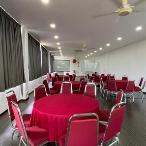 A conference room with round tables, red chairs, a whiteboard, and a projector screen.