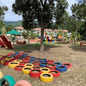 A playground with colorful tires arranged in a circle, a tree, and a building with a red roof in the background.