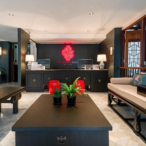 Un hall d'hôtel avec un comptoir d'accueil sombre, un panneau lumineux au néon et un espace détente comprenant un canapé et des fauteuils.