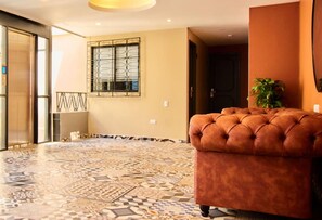 A room with a patterned floor, a tufted sofa, a potted plant, and a window with decorative metal bars. - Brana Hotel (Medellín)