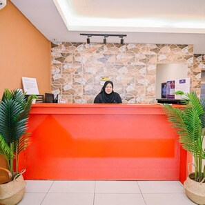 A reception desk with a stone wall backdrop, a person seated behind it, and potted plants on either side. - Swing & Pillows Myhome Wangsa Maju (Kuala Lumpur)