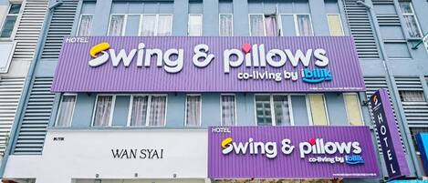 Un hotel con un letrero morado que dice 'Swing & Pillows' y un letrero 'Wan Syi' debajo.