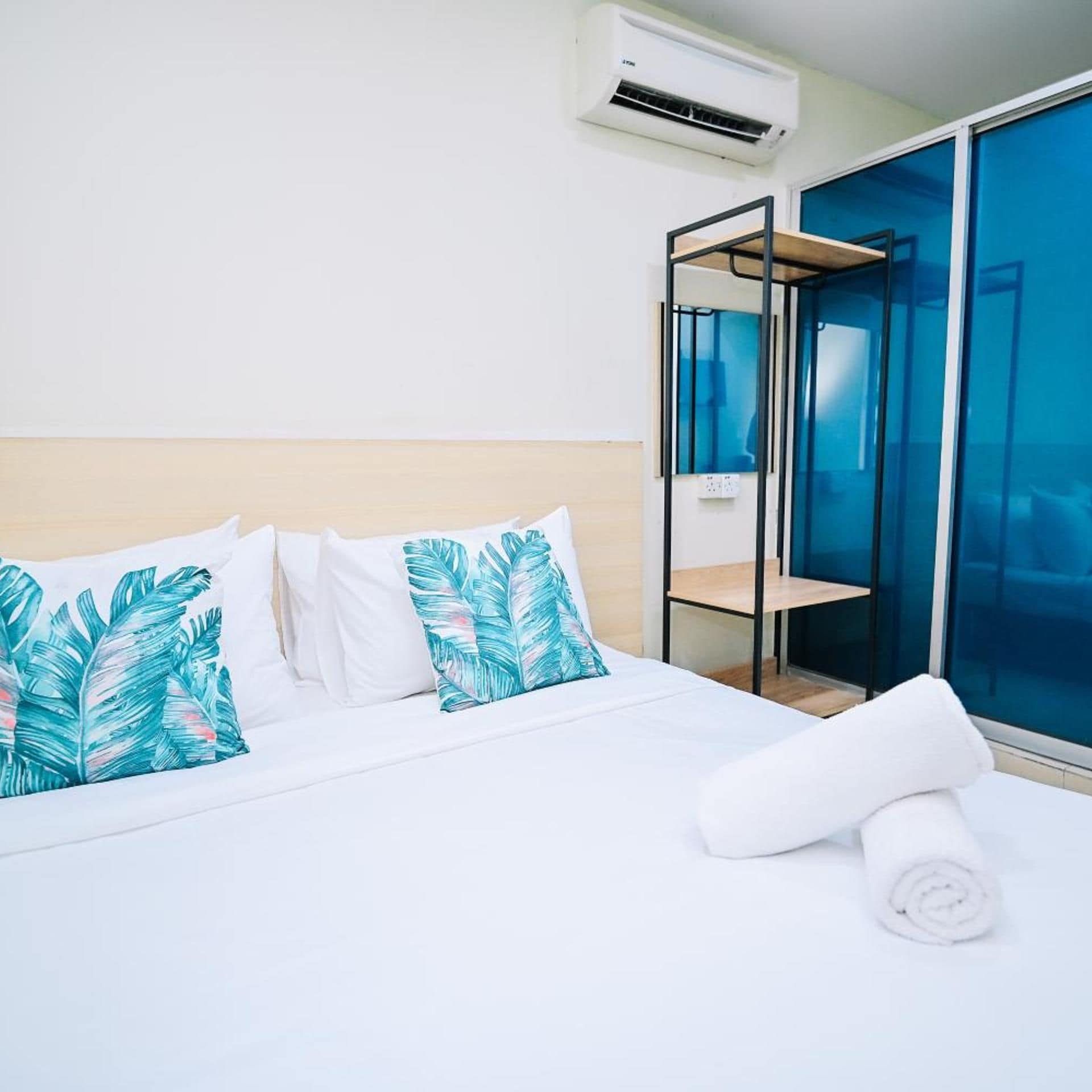 Une chambre d’hôtel avec un lit, du linge de lit blanc, une serviette enroulée, un appareil de climatisation et une cloison en verre.