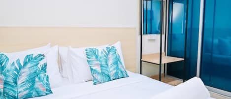 A hotel room with a bed, white bedding, a rolled towel, an air conditioning unit, and a glass partition.