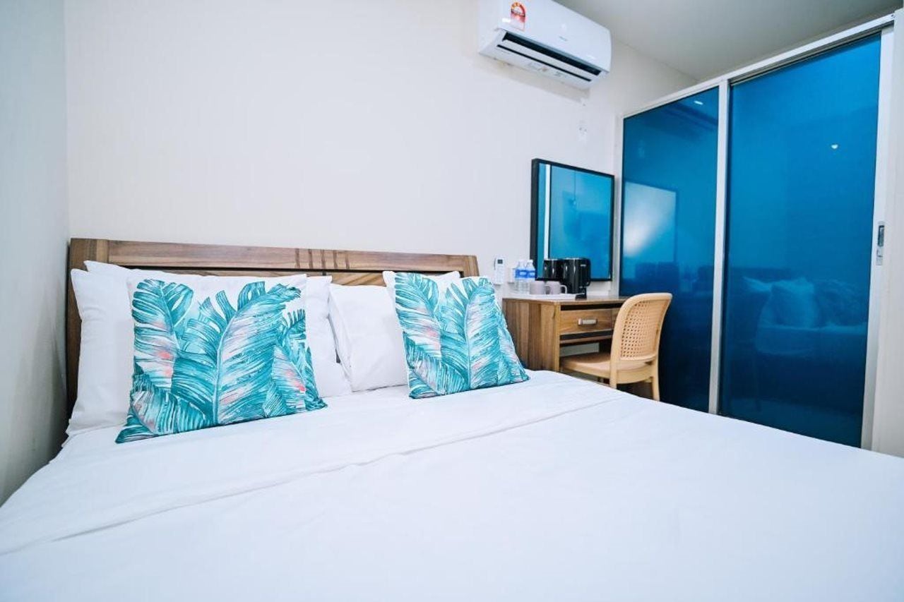 A hotel room with a bed, a desk, a chair, an air conditioning unit, and a large window.