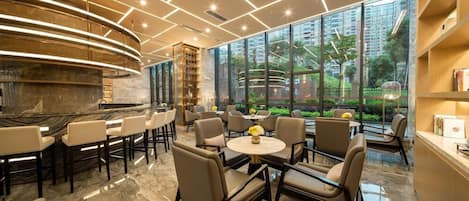A modern bar area with a curved counter, seating, and large windows offering a view of greenery.