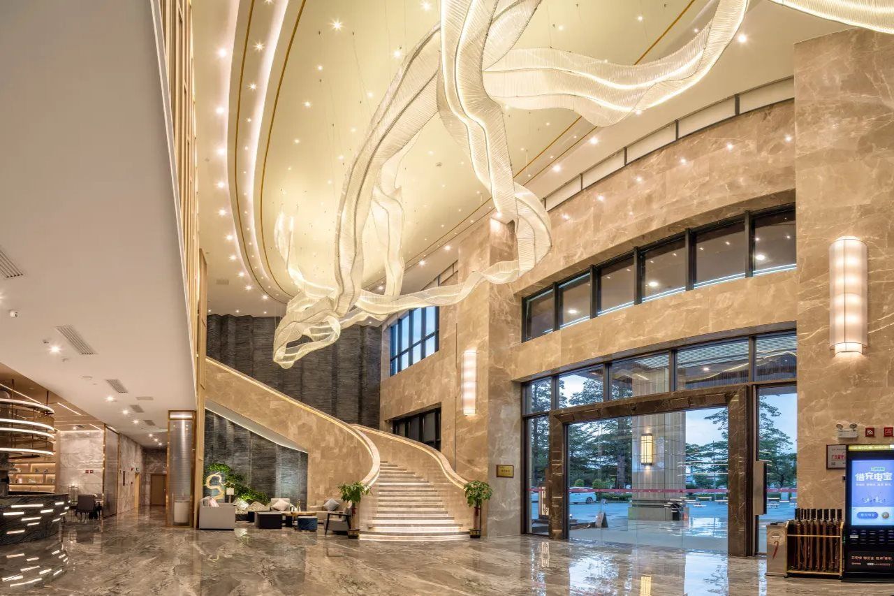 A spacious lobby with a grand staircase, a reception desk, and a large digital information screen.