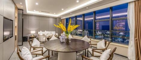 A modern dining area with a round table, white upholstered chairs, and a vase of yellow flowers.