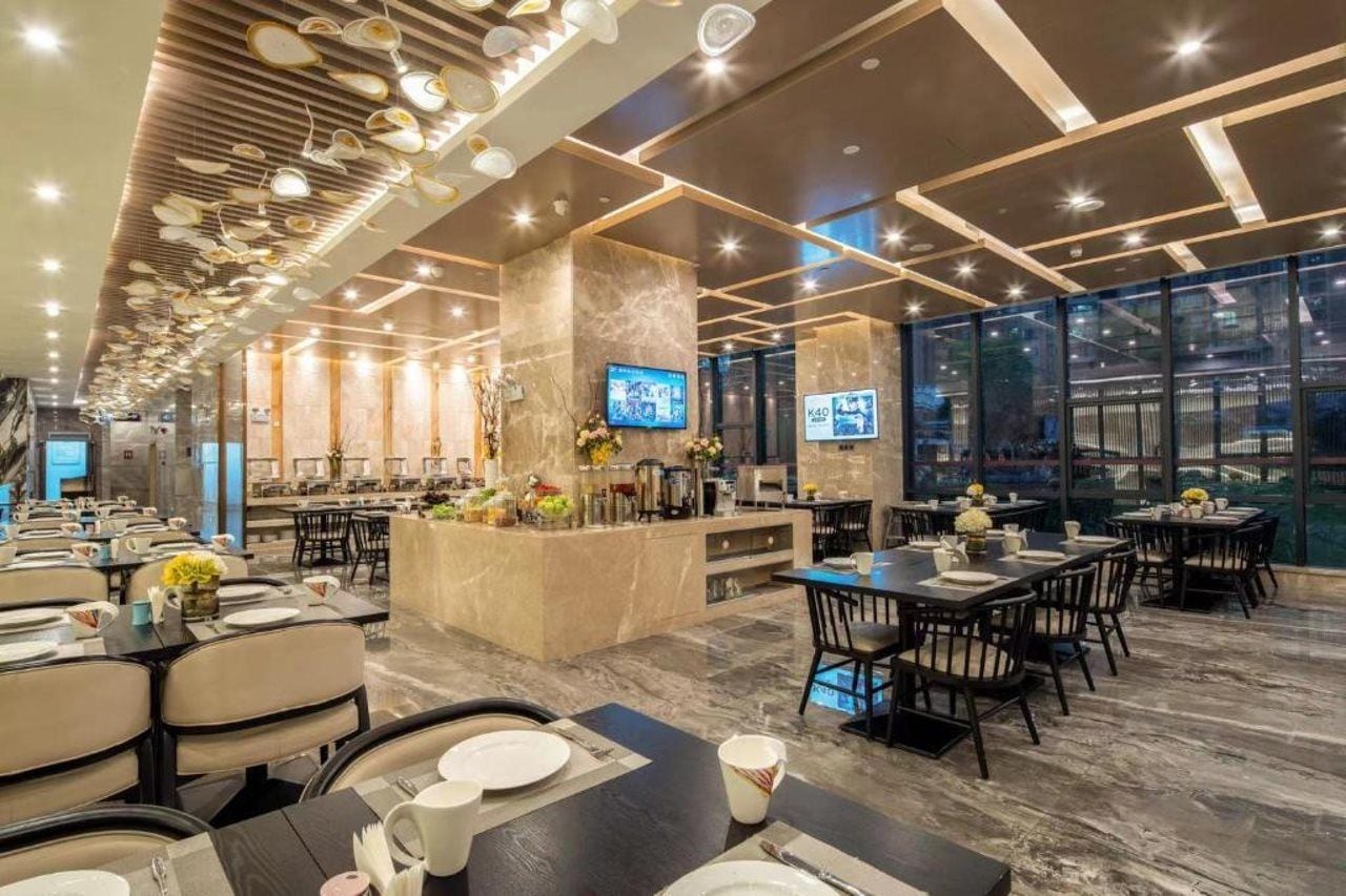 A modern restaurant with a long counter, multiple dining tables, and a TV screen.