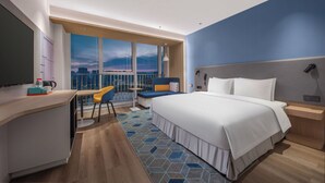 Habitación de hotel moderna con una cama grande, un escritorio, una silla y vistas de la ciudad a través de amplias ventanas.