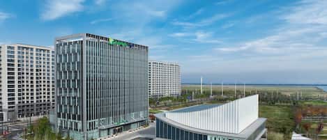 A modern building complex with a glass facade, surrounded by a landscaped area and a curved structure.