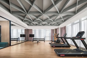 Une salle de sport moderne équipée de tapis de course, de poids et d’un grand miroir.