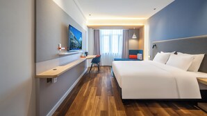 Habitación de hotel con una cama grande, un escritorio con silla, televisor y vistas al exterior por una ventana.