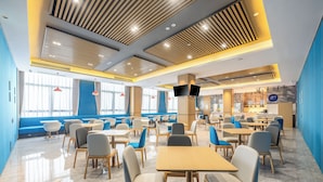 Un área de comedor moderna con varias mesas y sillas, una zona de estar azulada, y una cocina al fondo.