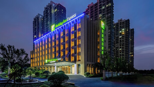 Un hotel de varios pisos con un llamativo letrero 'Holiday Inn Express', un acceso cubierto y vegetación circundante.