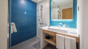 Un baño moderno con cabina de ducha de vidrio, un lavamanos blanco y un espejo grande con revestimiento de azulejos azules.