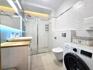 A modern bathroom with a glass-enclosed shower, a toilet, and a washing machine. - Apartament Nicole by Q4 Apartments  (Gdynia)