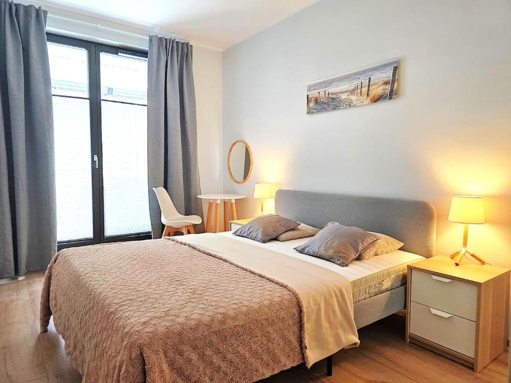 A bedroom with a bed, bedside tables, a chair, a painting, and a window with curtains.