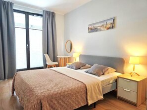 A bedroom with a bed, bedside tables, a chair, a painting, and a window with curtains. - Apartament Nicole by Q4 Apartments  (Gdynia)