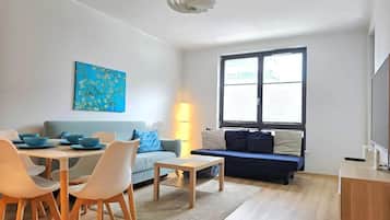 A modern living room with a dining area, a sofa, a TV, and a painting on the wall.