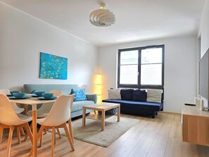 A modern living room with a dining area, a sofa, a TV, and a painting on the wall. - Apartament Nicole by Q4 Apartments  (Gdynia)