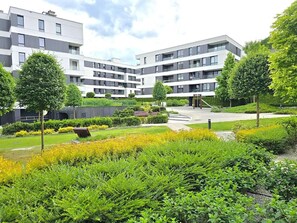 Ein modernes Mehrfamilienhaus mit angelegtem Garten, einem Spielplatz und blauem Himmel.