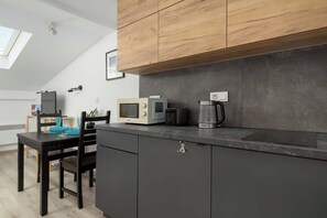 Une cuisine moderne avec des meubles de couleur sombre, un plan de travail en bois, un four à micro-ondes, une machine à café et un coin repas avec une table et des chaises.