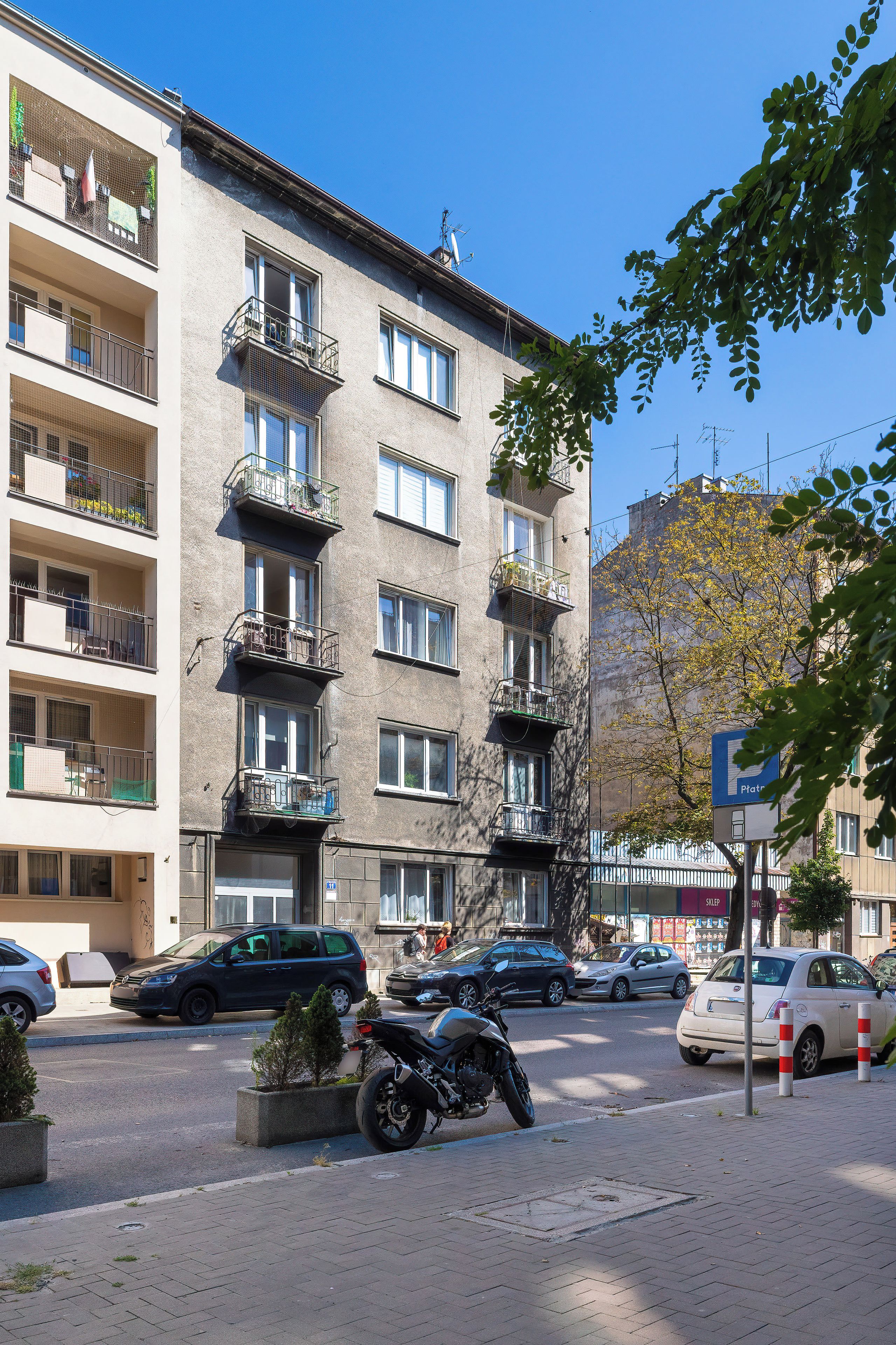 Un immeuble à plusieurs étages doté de balcons, avec des voitures garées et une moto dans la rue.