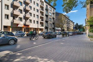 En byggnad med flera våningar, där det finns ett apotek på bottenvåningen, en cykelbana och parkerade bilar.