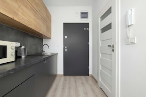 A modern kitchen with a microwave, kettle, and coffee maker. There is a dark door with a lock and a white wall-mounted phone. - Cracow | 11 Mazowiecka Street | Cosy Studio | Air conditioning (Kraków)