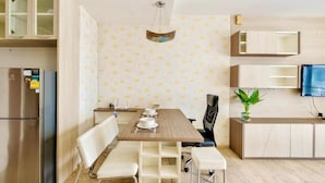 A modern kitchen with a wooden table, white chairs, a built-in oven, and a television on the wall. - Noble Remix Bangkok (Krung Thep Maha Nakhon)