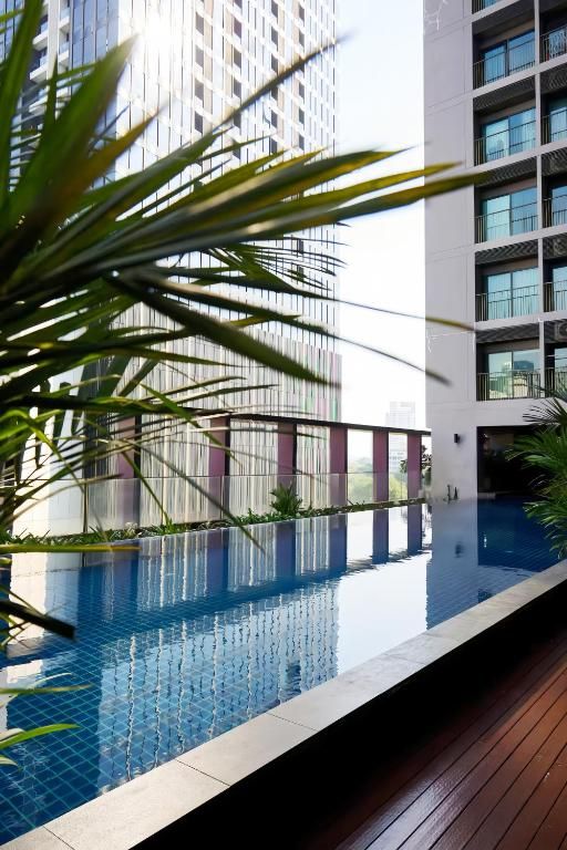 A modern building with a rooftop pool, surrounded by greenery and a clear view of a tall building in the background.