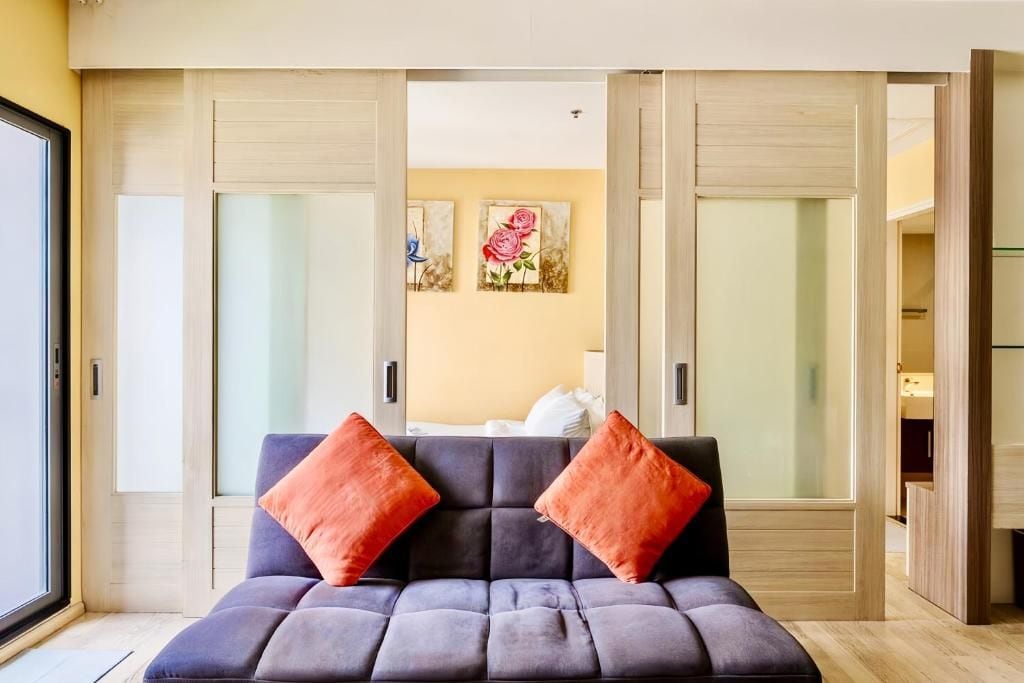 A modern room with a grey sofa, two red cushions, a bed with white bedding, and a wall with two framed floral paintings.