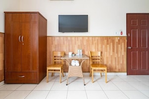 Quarto com guarda-roupa de madeira, televisão fixada na parede, pequena mesa com cadeiras e porta de madeira.