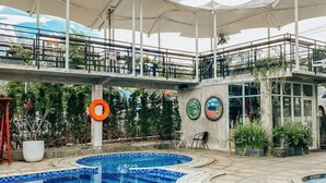Une piscine avec un bord carrelé, une bouée de sauvetage et un espace détente couvert équipé de parasols.