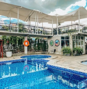 A swimming pool with a tiled edge, a lifebuoy, and a covered seating area with umbrellas. - Bells Place Hotel (Cijayanti)