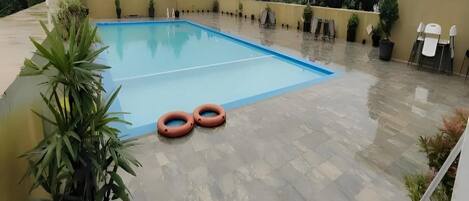A rooftop pool area with a blue pool, potted plants, and outdoor seating.