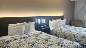 Habitación de hotel con dos camas, una mesita de noche con teléfono y despertador, y una silla.