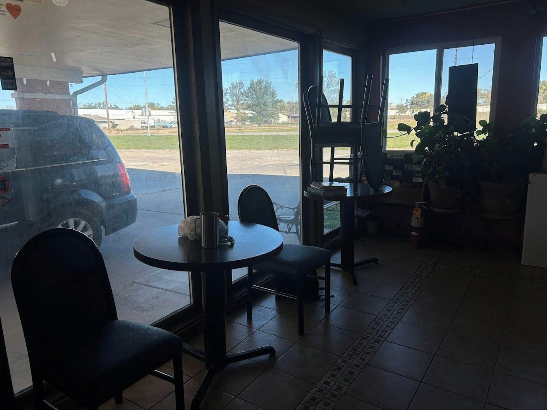 Une pièce avec une table et des chaises, une fenêtre donnant sur un parking et une plante.