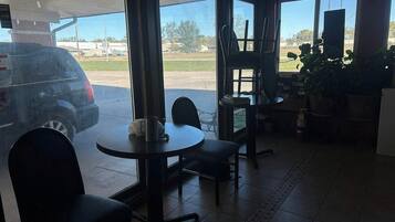 Une pièce avec une table et des chaises, une fenêtre donnant sur un parking et une plante.